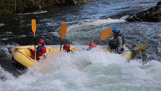 ラフティングツアーで楽しむ家族や団体のお客様の集合写真。北海道の豊かな自然と爽やかな青空をバックに記念撮影。