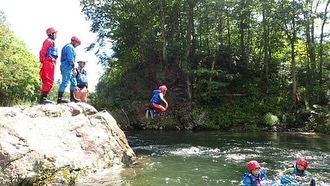 北海道の自然の中で、崖から川にジャンプするラフティングツアー参加者のアクティビティ風景。冒険心をくすぐるアウトドア体験。