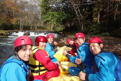 北海道のラフティングツアーでボートに乗り、リラックスしながら秋の景色を楽しむ参加者たち。美しい渓流をバックにしたアクティビティ。