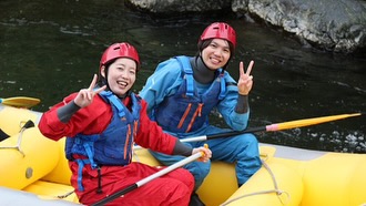 北海道のラフティングツアーで、ボート上でピースサインをする笑顔の参加者。初心者でも安心して楽しめるガイド付き。