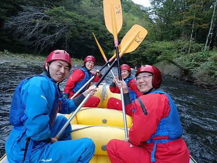 北海道のラフティングツアーでボートに乗り、パドルを手に笑顔を見せる参加者たち。仲間と楽しむアウトドア体験。